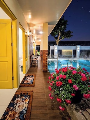 A corridor leading to a pool area with a wooden floor, a potted plant with flowers, and a seating area with chairs and a table. - Palma Villa Homestay Klaten (Klaten)
