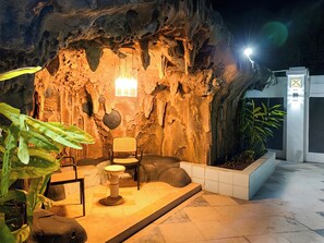 An outdoor seating area with a rock wall backdrop, a table, chairs, and potted plants.
