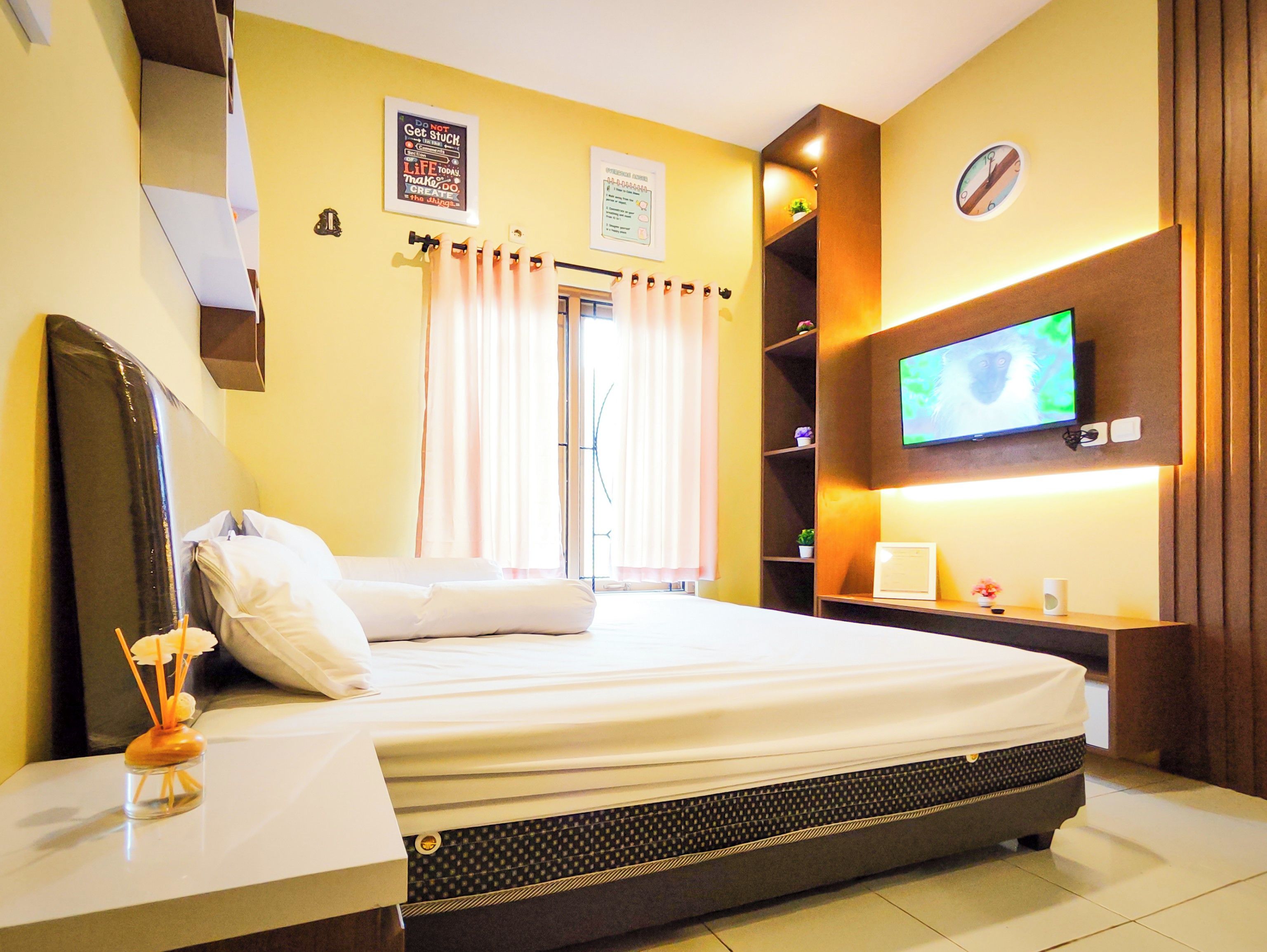 Habitación de hotel con una cama, televisión, estante con adornos y ventana con cortinas.