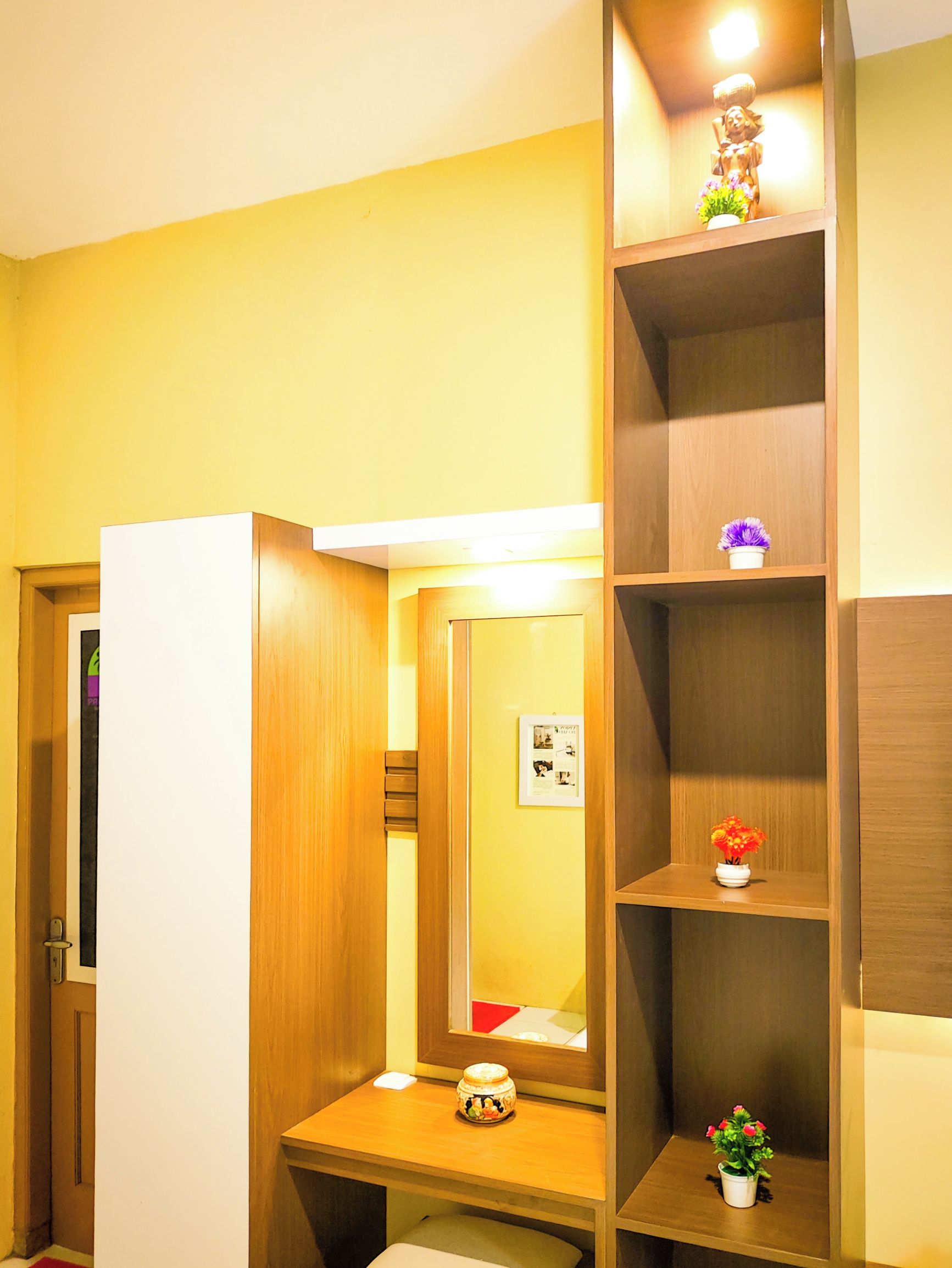 Una habitación con tocador de madera, un espejo y repisas con objetos decorativos.