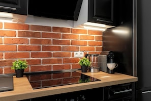 Eine Küche mit Backsteinwand, einer schwarzen Induktionskochplatte, einer Kaffeemaschine und einem Blumentopf.