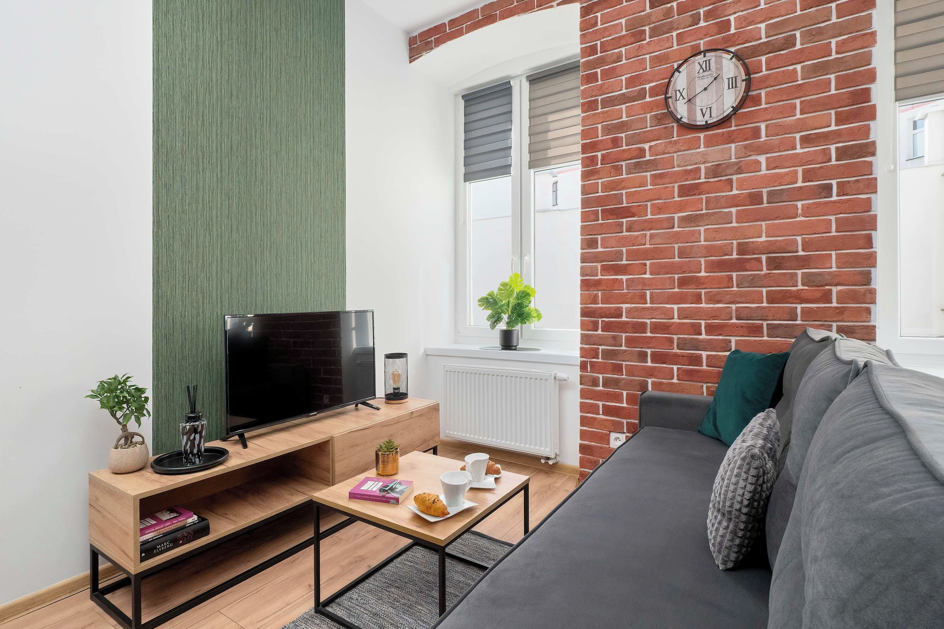 Ein modernes Wohnzimmer mit Flachbildfernseher, Couch, Couchtisch und einer Ziegelwand mit Uhr.