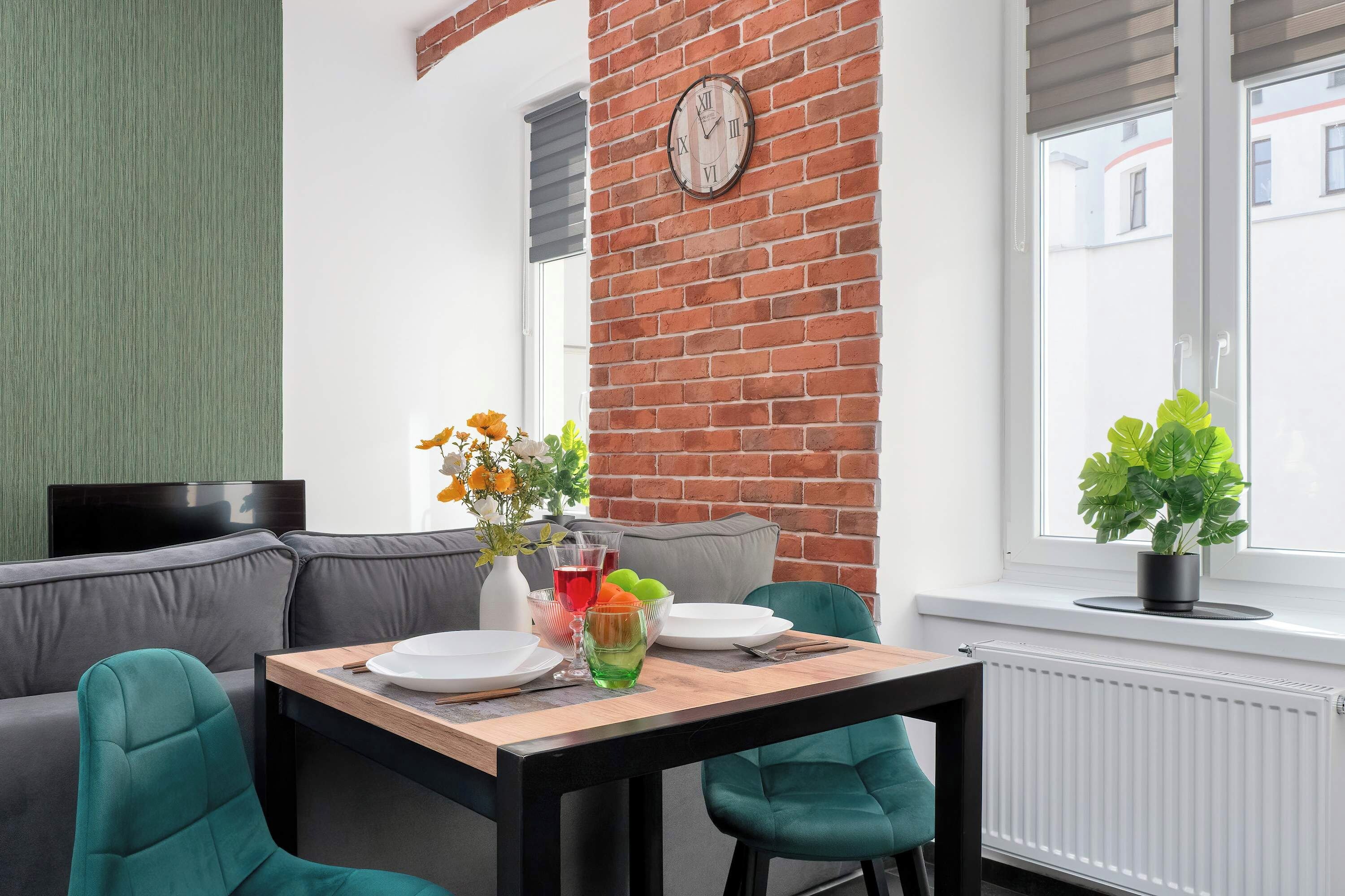 Ein modernes Wohnzimmer mit Backsteinwand, einer Couch, einem Esstisch mit Stühlen und einem Fenster mit Jalousien.