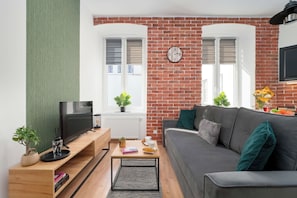 Ein Wohnzimmer mit Backsteinwand, einer Couch, einem Fernseher und einer Uhr.