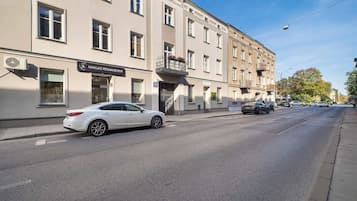 Straßenansicht mit einem weißen Auto, das vor einem Gebäude mit der Aufschrift 'MAKIJAŽ PERMANENTNY' geparkt ist.