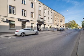 Straßenansicht mit einem weißen Auto, das vor einem Gebäude mit der Aufschrift 'MAKIJAŽ PERMANENTNY' geparkt ist.