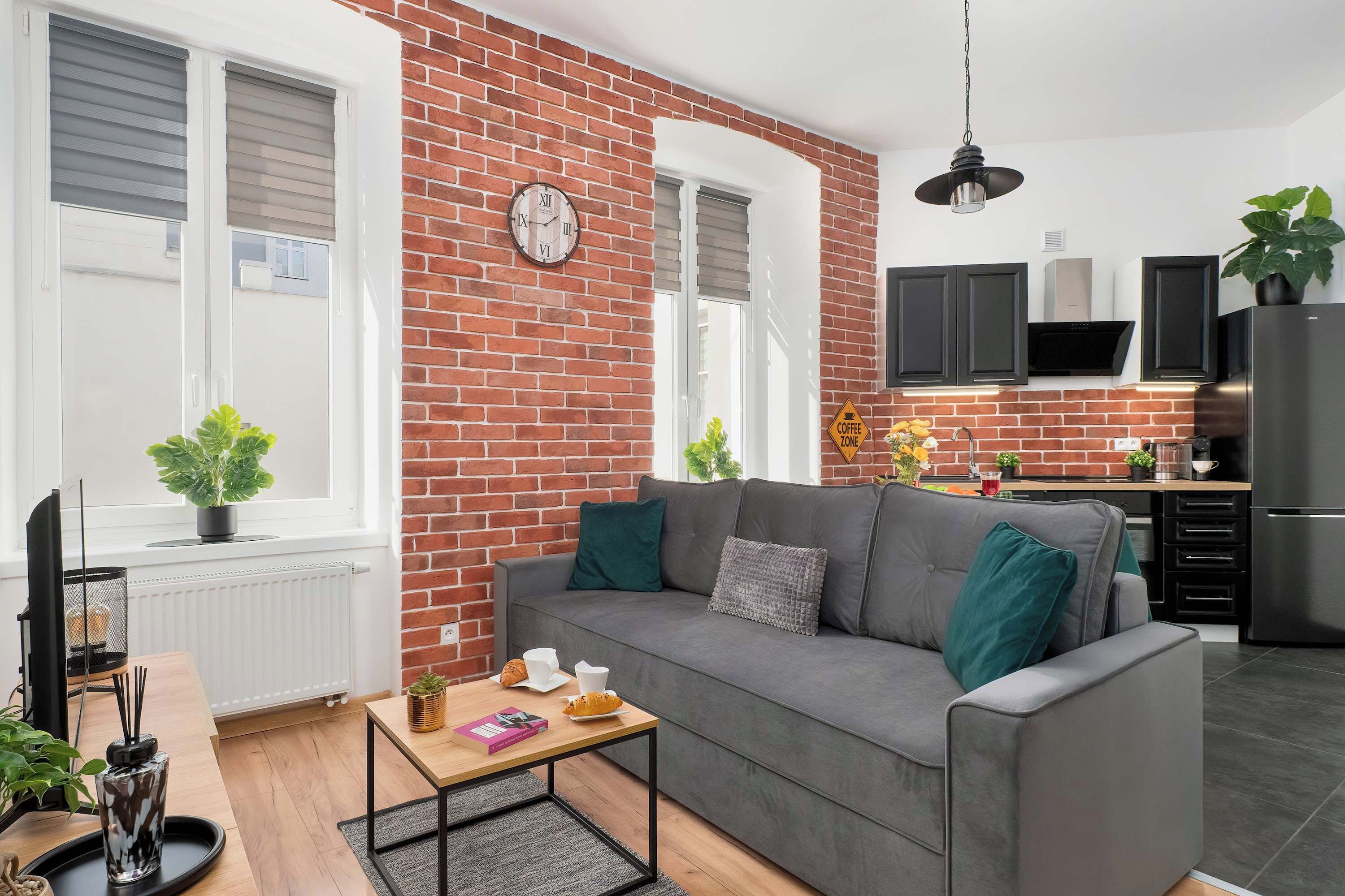 Ein modernes Wohnzimmer mit grauem Sofa, Couchtisch und Backsteinwand.