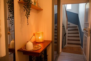 A hallway with a wooden table, a lamp, and a staircase. - Winds from the Open Sea (Cancale)