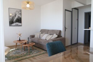 A modern living room with a sofa, a small table with a bottle and glass, a starfish decoration, and a framed picture on the wall. - Winds from the Open Sea (Cancale)
