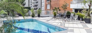 Una piscina con sillones de descanso y plantas en macetas en un patio.
