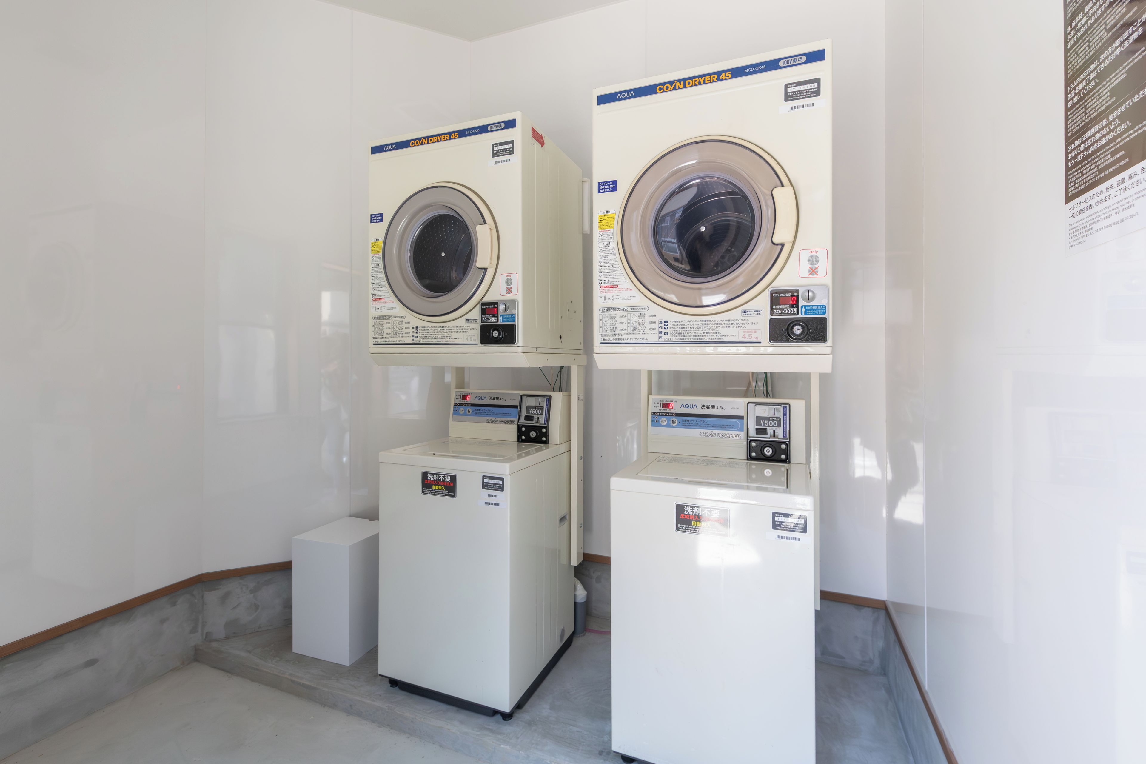 Two stacked front-loading washing machines in a laundry room with a tiled floor and white walls.
