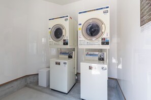 Deux machines à laver à chargement frontal, superposées, dans une buanderie avec un sol carrelé et des murs blancs.