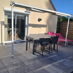 A patio with a table and chairs, a sliding glass door, and a covered area with a roof. - La Fontaine du Marais Vacation Rental, located near St. Valery-sur-Somme, with free parking (Pendé)