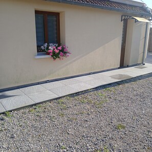 A building with a window, a flower box with pink flowers, and a gravel driveway. - La Fontaine du Marais Vacation Rental, located near St. Valery-sur-Somme, with free parking (Pendé)