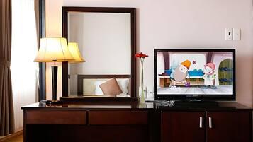 A hotel room with a television, a lamp, a mirror, and a vase with flowers.