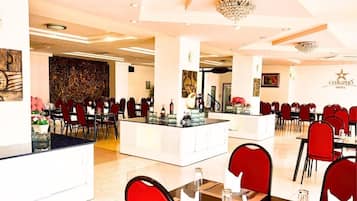 Un comedor de hotel con varias mesas y sillas, una isla central con barra y obras de arte en las paredes.