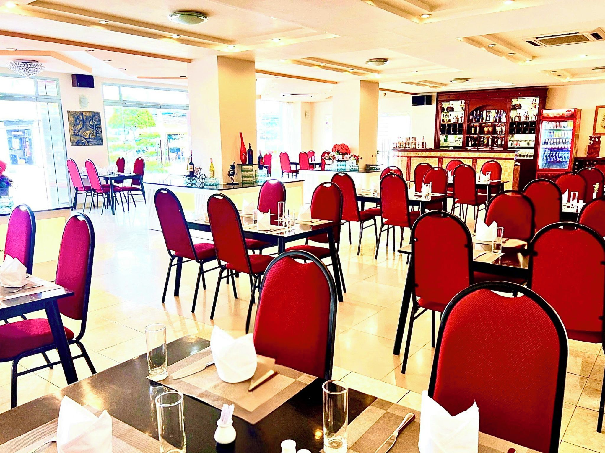 En restaurang med röda stolar och bord, en bardisk och utsikt över omgivningarna.