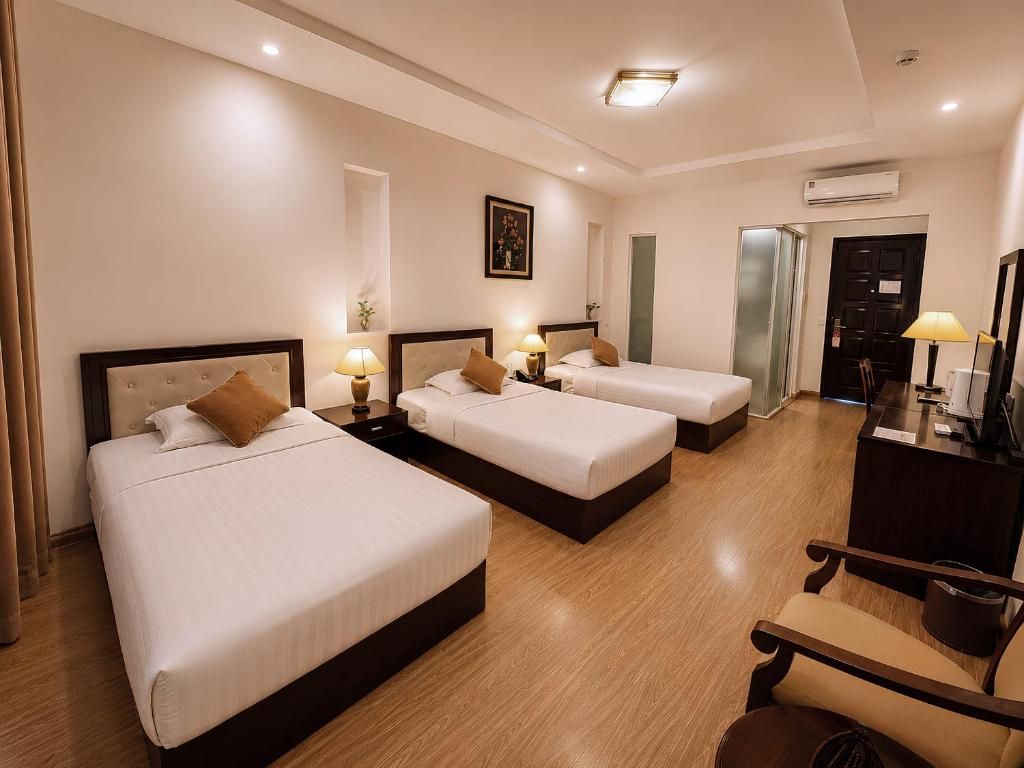 A hotel room with three beds, a desk, and a chair.