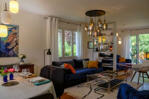 A modern living room with a sofa, coffee table, and dining area with a table set for two. - Ty Maine (Saint-Malo)