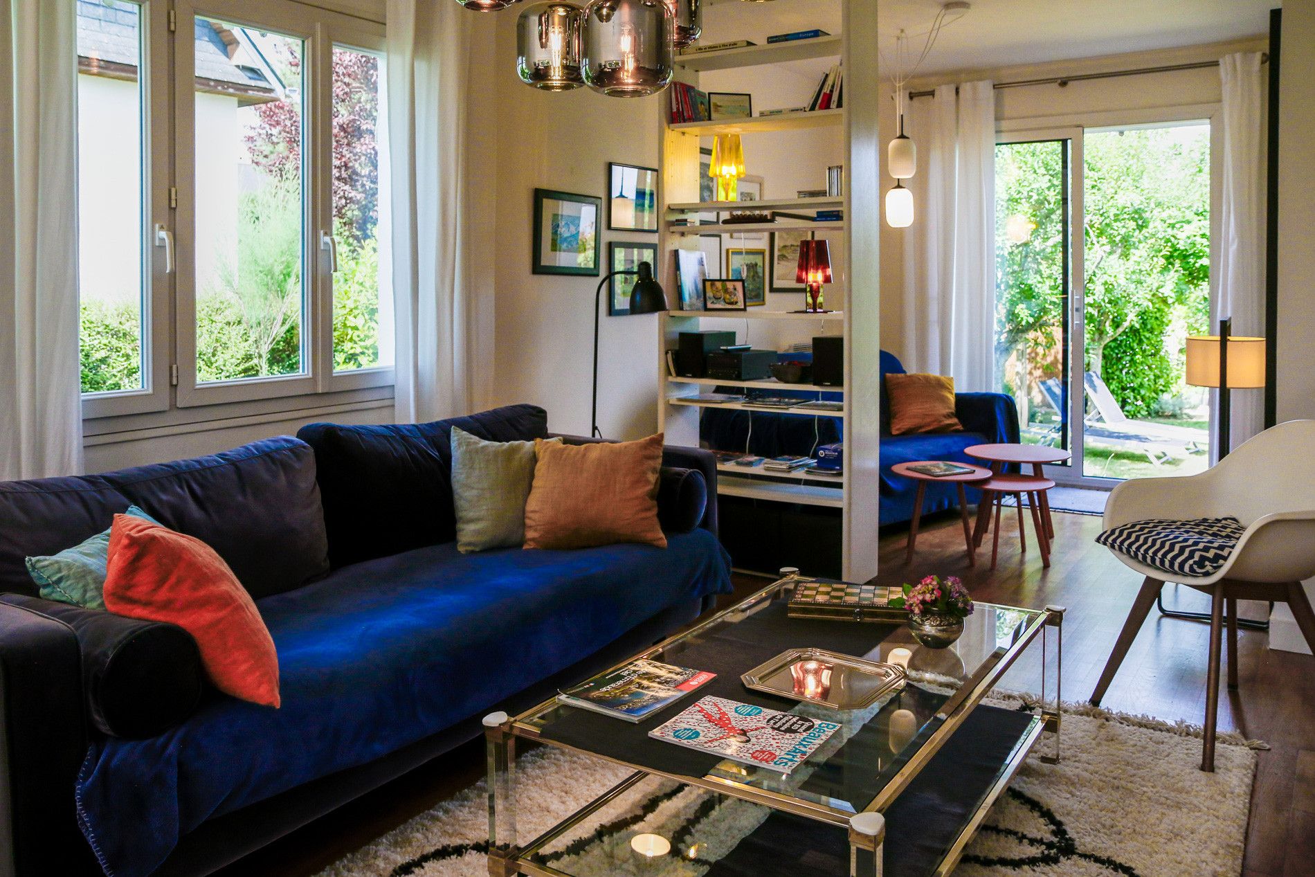 A modern living room with a blue sofa, a glass coffee table, and a bookshelf.