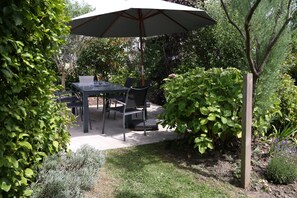 An outdoor patio with a table and chairs, surrounded by lush greenery and a wooden post. - Ty Maine (Saint-Malo)