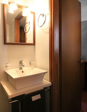 Un bany amb un lavabo blanc, un mirall i una porta de fusta.