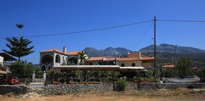 A coastal property with a stone wall, a red car, and a sailboat. - Xenios Apartments (West Mani)