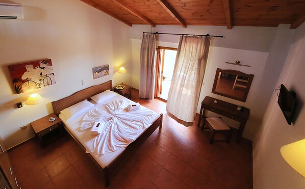 A bedroom with a wooden bed, a bedside table, a desk, a chair, a mirror, and a window with curtains. - Xenios Apartments (West Mani)