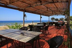 An outdoor seating area with tables and chairs, overlooking a beach and the sea. - Xenios Apartments (West Mani)