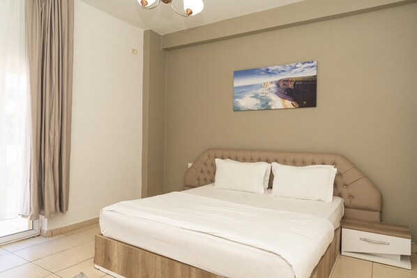 A hotel room with a bed, a nightstand, a painting on the wall, and a window with curtains. - Hotel Princ (Golem)
