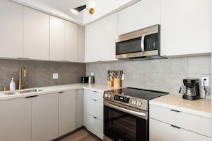 Eine moderne Küche mit weißen Schränken, einer Edelstahl-Mikrowelle, einem eingebauten Backofen und einer Kaffeemaschine.