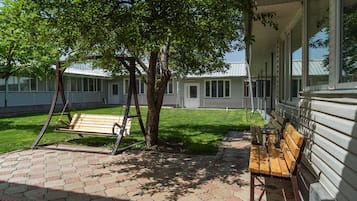 Een terras met een schommelset, een bank en een boom die schaduw geeft.