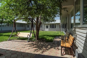 A patio area with a swing set, a bench, and a tree providing shade.
