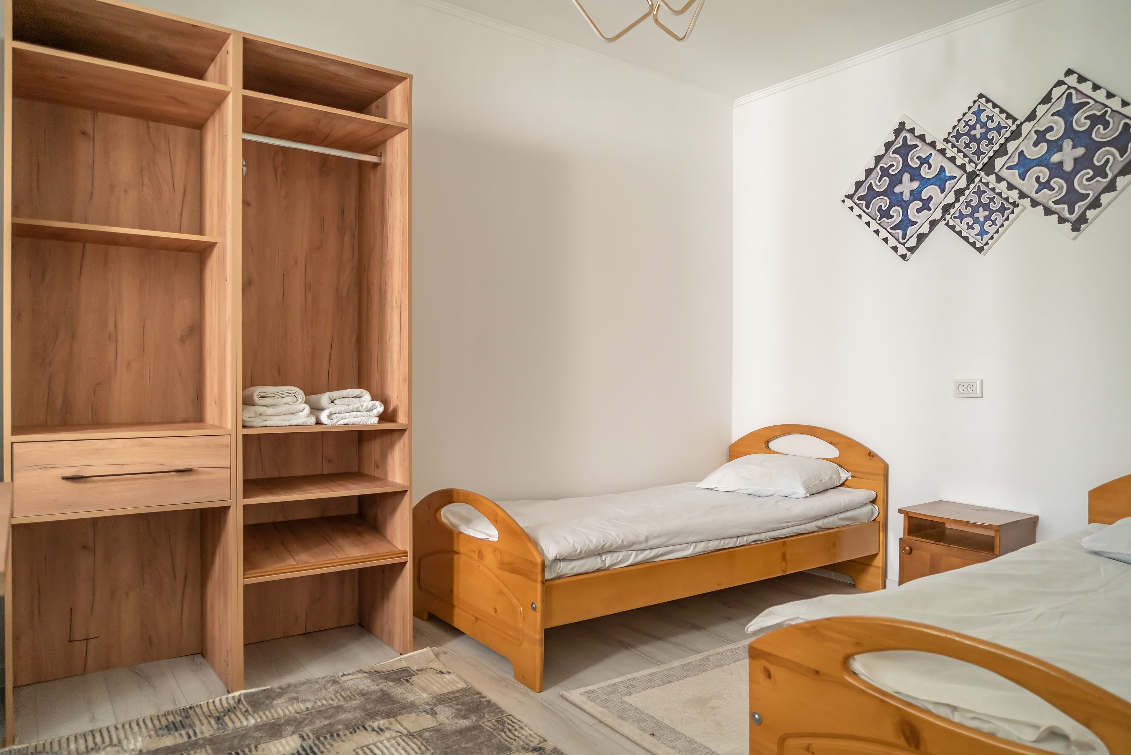 A bedroom with a wooden bed, a wooden wardrobe, a small bedside table, and a patterned rug.