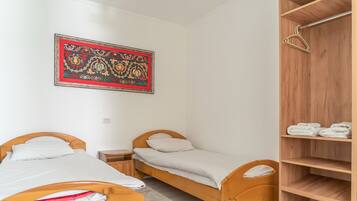 A small, clean room with two wooden beds, a wooden wardrobe, and a decorative wall hanging.