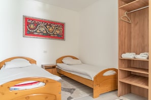 A small, clean room with two wooden beds, a wooden wardrobe, and a decorative wall hanging.