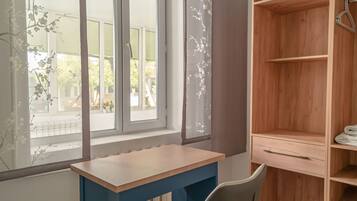 Een kamer met een houten bureau, een stoel, een raam met uitzicht op groen en een houten kledingkast.