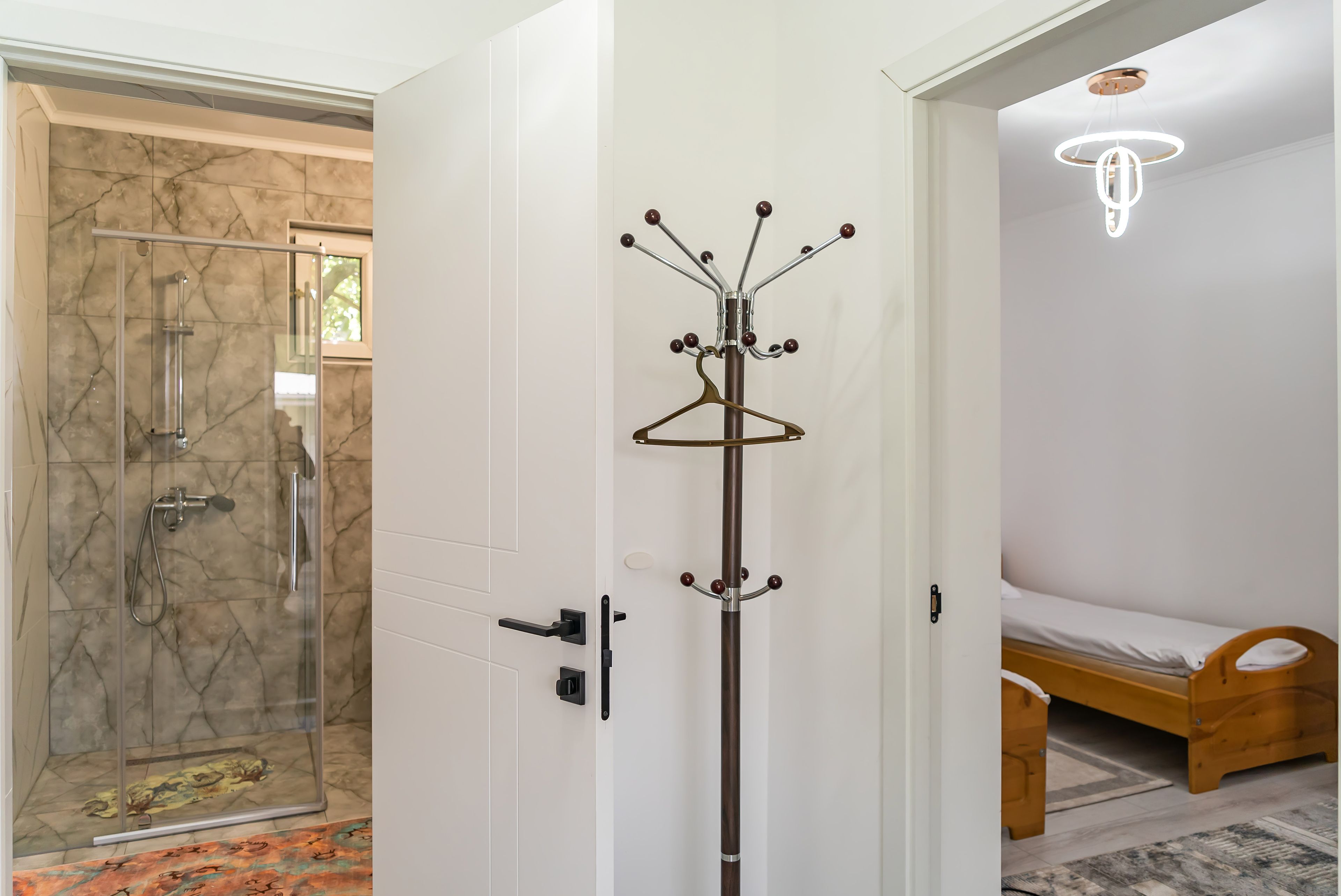 A room with a glass shower enclosure, a coat rack, a bed, and a hanging light fixture.