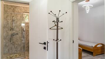 A room with a glass shower enclosure, a coat rack, a bed, and a hanging light fixture.
