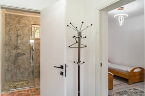 A room with a glass shower enclosure, a coat rack, a bed, and a hanging light fixture.