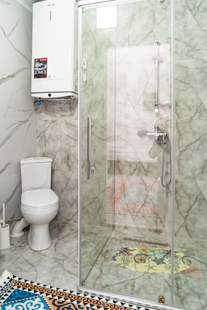 A bathroom with a toilet, a shower enclosure, and a marble-tiled floor.