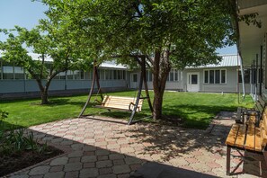 Un espace extérieur aménagé avec une balançoire, un banc et un chemin pavé.