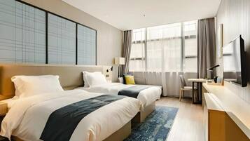 A hotel room with two beds, a desk, a chair, a TV, and large windows.
