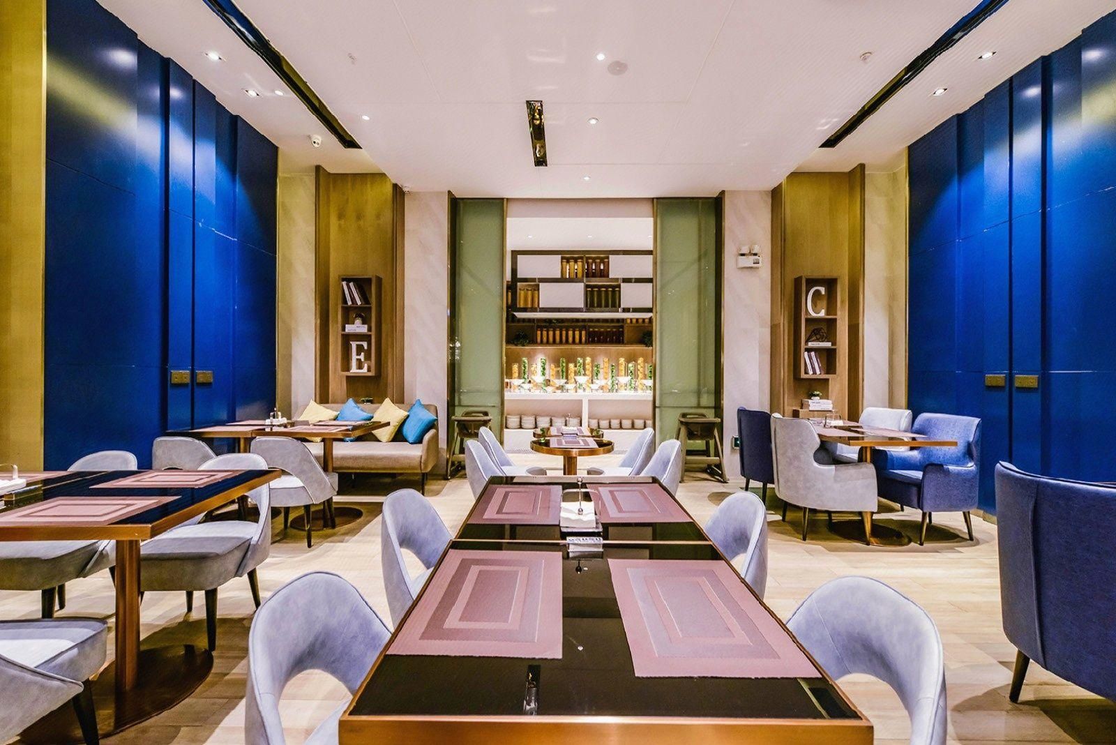 A modern hotel lobby with a central seating area, a reception desk, and a bookshelf with decorative items.