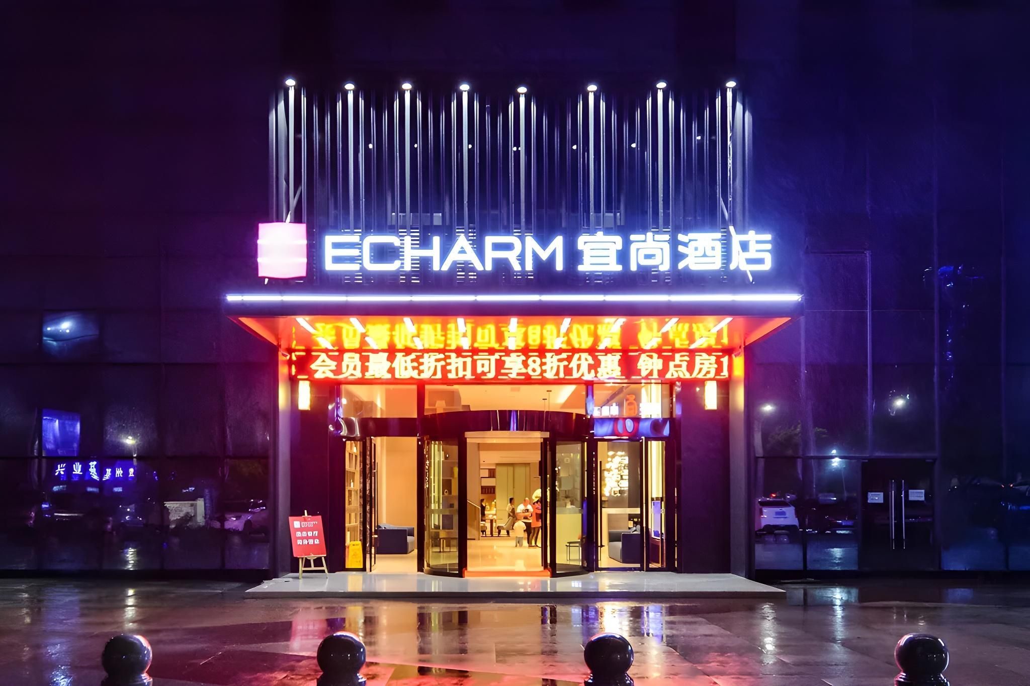 A hotel entrance with a prominent sign, glass doors, and a wet pavement.