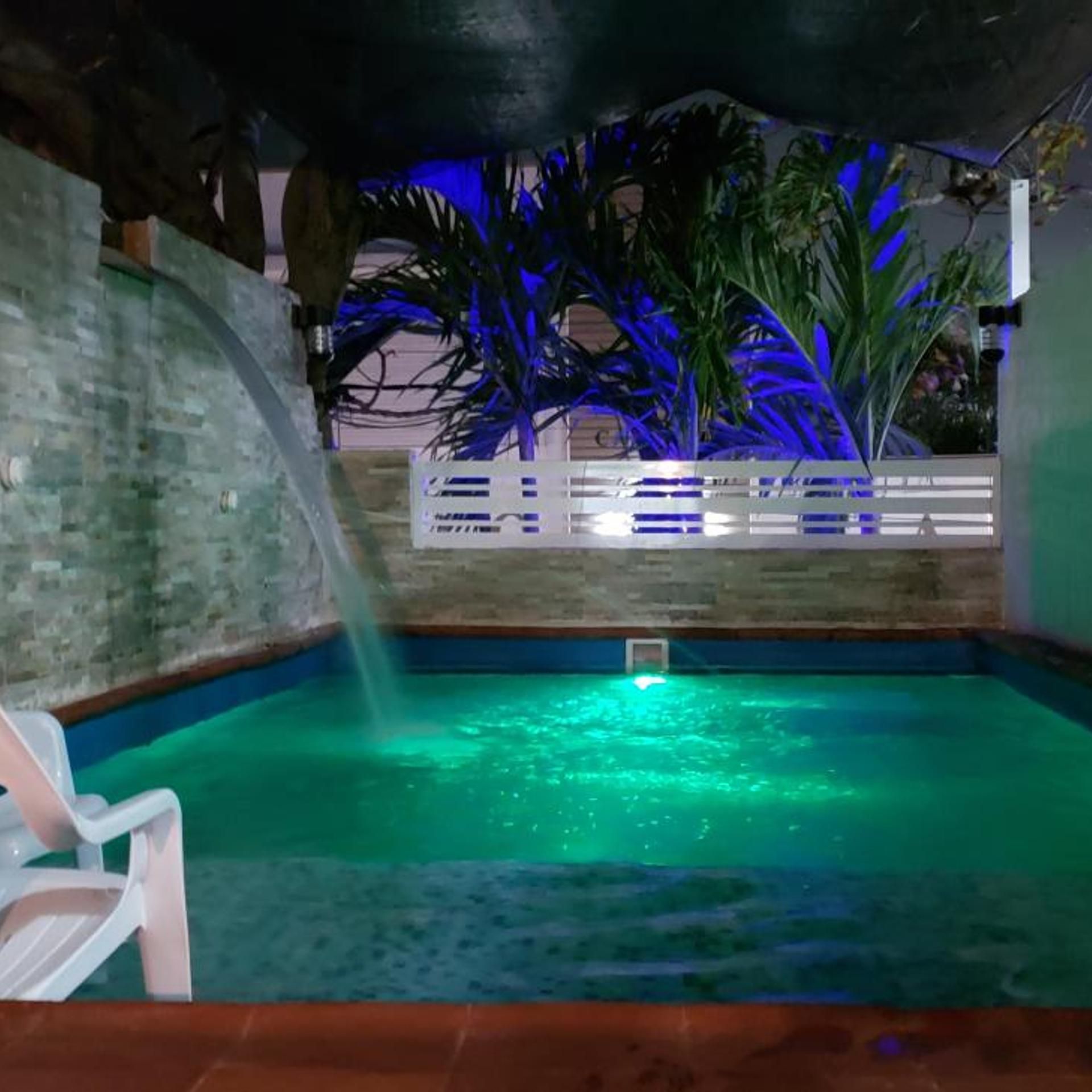 A swimming pool with a waterfall feature, surrounded by a brick wall and palm trees.