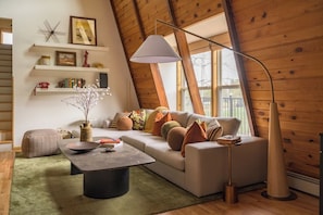 Una sala de estar acogedora con un sofá, una mesita de centro y una lámpara. Hay estantes con objetos decorativos y una ventana con vistas.