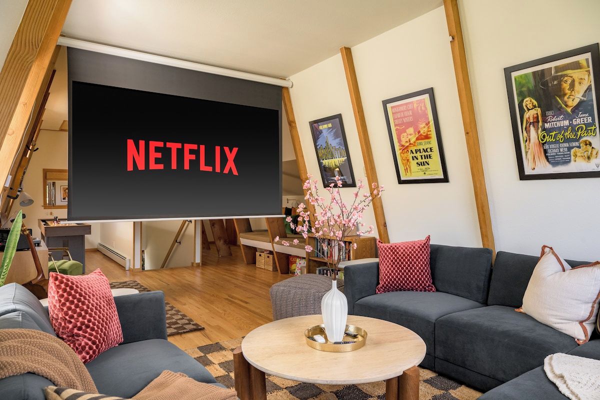 A living room with a large screen displaying 'NETFLIX,' a sofa, a coffee table, and a bookshelf.