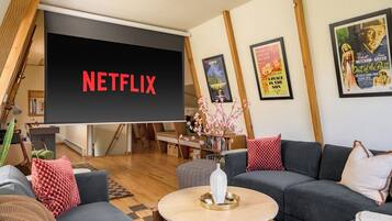 A living room with a large screen displaying 'NETFLIX,' a sofa, a coffee table, and a bookshelf.