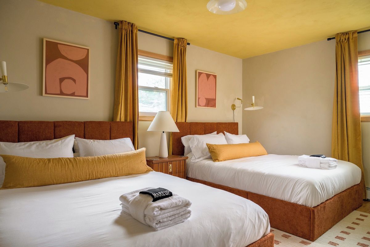 A hotel room with two beds, a nightstand, a lamp, and artwork on the walls.